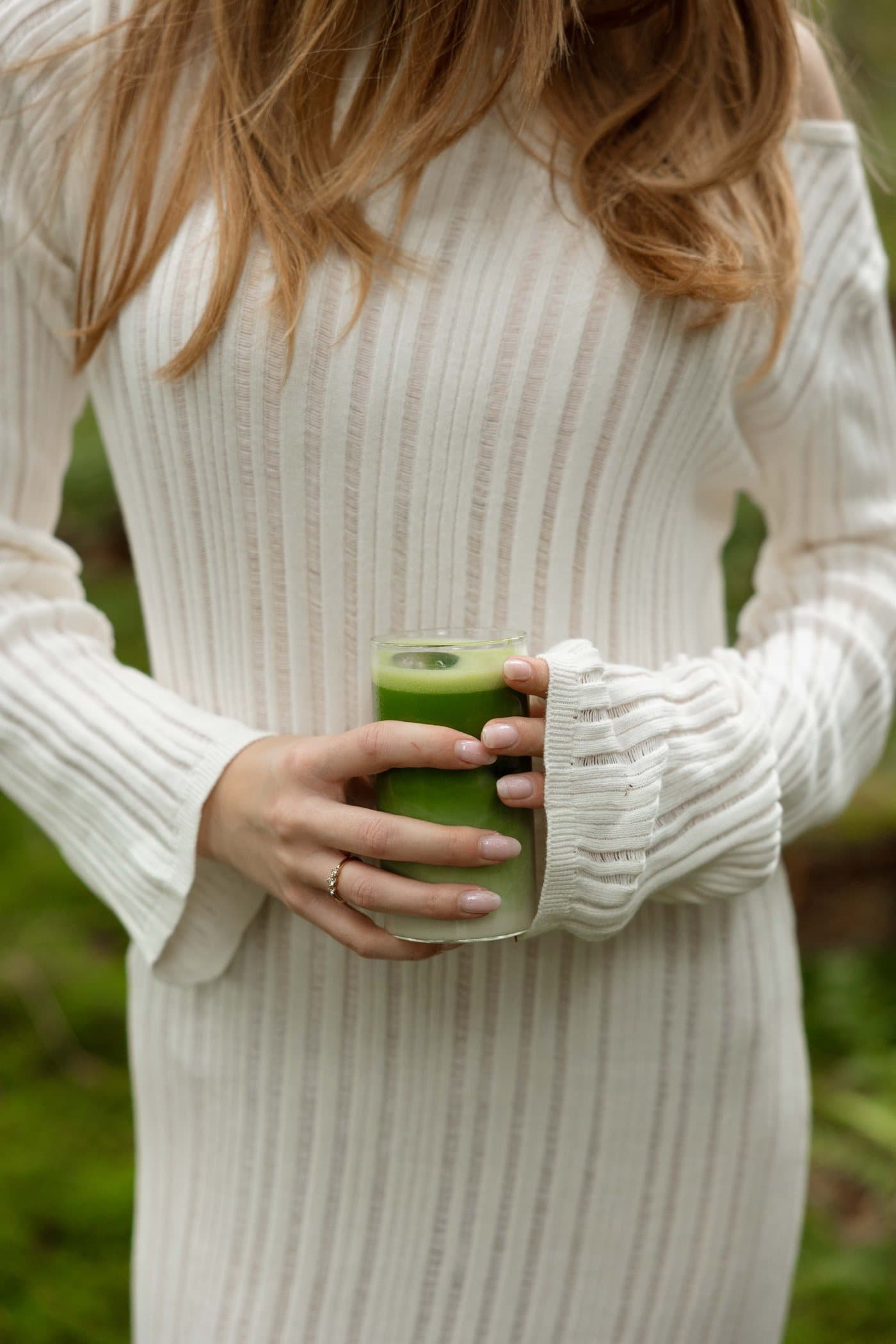 Someone in a cream knitted dress holding a glass of iced matcha latte